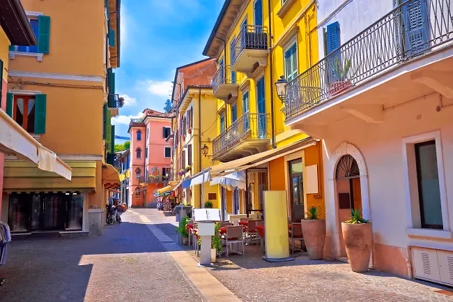 Een bestrate straat met okergele en rode huizen, balkons en terrassen in het centrum van Peschiera del Garda